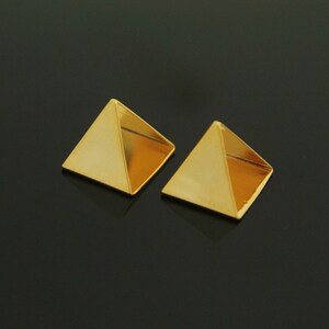 May include: A pair of gold pyramid-shaped earrings. The earrings are small and have a shiny finish.