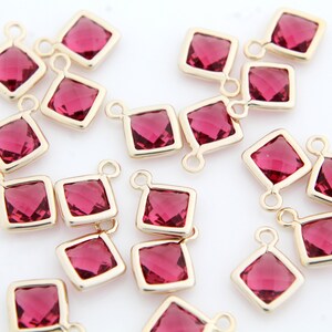 Puede incluir: Un grupo de 16 abalorios cuadrados de color dorado con un cristal rojo en el centro. Cada abalorio tiene un bucle en la parte superior para sujetarlo a joyas.