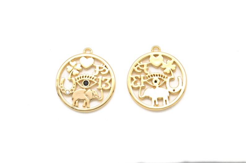 May include: Two gold-colored round pendants with various cut-out designs. Each pendant features an eye, elephant, horseshoe, heart, and four-leaf clover. One pendant has the number 13. The pendants have a small loop at the top for hanging.