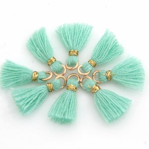May include: A set of eight mint green tassels with gold accents. Each tassel has a gold ring attached to the top.