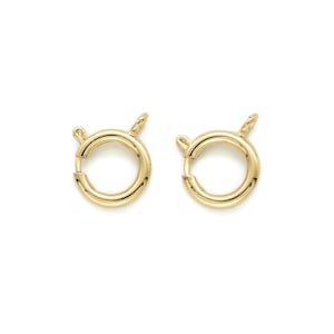 Puede incluir: Dos cierres de metal dorado para la elaboración de joyas. Cada cierre es un círculo redondo con un pequeño bucle en la parte superior.