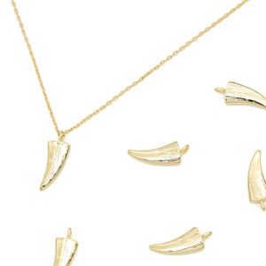 Puede incluir: Un collar de oro con un colgante con forma de diente. El colgante es texturizado y tiene un acabado brillante. Hay varios colgantes con forma de diente dispersos alrededor del collar.