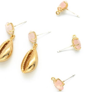 May include: Gold-tone seashell dangle earrings with a light pink gemstone accent. The earrings have a post-back closure. Several pairs of earrings are scattered on a white background.