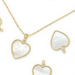 May include: A gold chain necklace with multiple heart-shaped pendants. Each pendant is made of white mother-of-pearl and has a small clear rhinestone in the center.