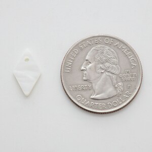 May include: A white, diamond-shaped shell pendant with a hole at the top. The pendant is about the size of a US quarter.