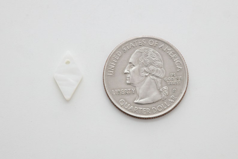 May include: A white, diamond-shaped shell pendant with a hole at the top. The pendant is about the size of a US quarter.
