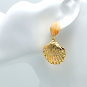 Op de afbeelding: Gouden schelpvormige oorbellen met een perzikkleurige ovale kraal aan de bovenkant.