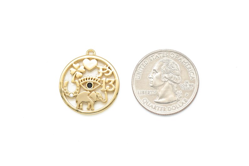 May include: Gold-colored charm with a circular design featuring a heart, four-leaf clover, horseshoe, elephant, and the number 13. A U.S. quarter is next to the charm for size comparison. The charm has a small loop at the top for hanging.