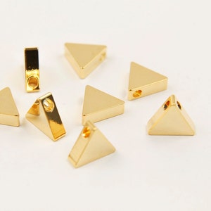 May include: Seven gold-coloured triangle-shaped metal charms with a hole in the centre of each charm.