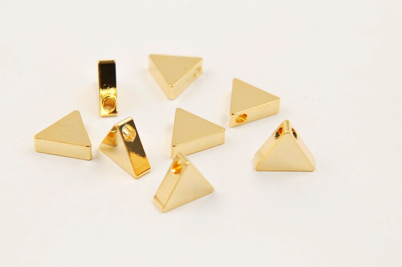 May include: Seven gold-coloured triangle-shaped metal charms with a hole in the centre of each charm.