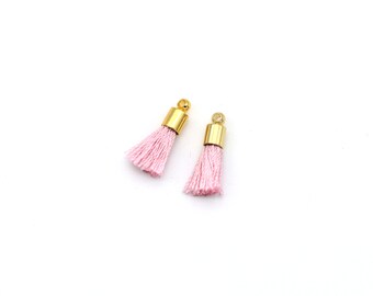 May include: Two pink tassel charms with gold metal caps. The tassels are made of soft, fluffy fibers.
