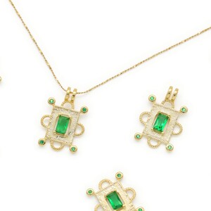 May include: A gold chain necklace with multiple green gemstone pendants. Each pendant features a square green gemstone surrounded by a gold frame with intricate details.