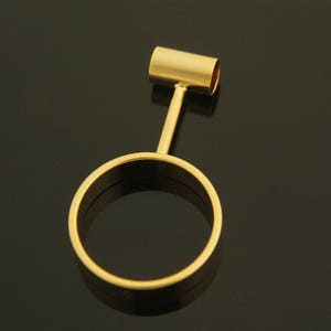 May include: A gold-colored metal ring with a vertical bar attached to the top. The ring is round and has a smooth surface.