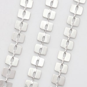 Puede incluir: Tres hilos de una cadena plateada con un patrón repetitivo de eslabones cuadrados conectados por un óvalo alargado. Los eslabones son planos y tienen un acabado de metal cepillado, creando un diseño geométrico moderno.