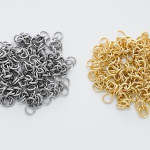 Könnte beinhalten: Zwei Stapel Sprungringe, einer silber und einer gold. Die Sprungringe sind klein und rund und perfekt für die Schmuckherstellung.