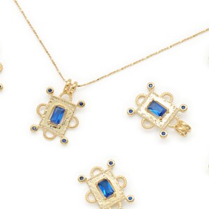 May include: A gold chain necklace with multiple blue gemstone pendants. Each pendant is a square with a blue gemstone in the center and a decorative gold frame.