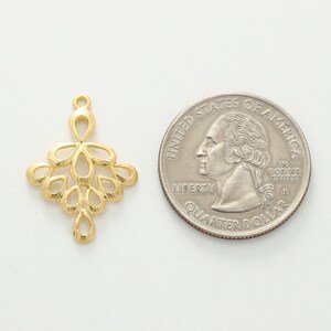 May include: Gold-toned metal pendant with a delicate, intricate design resembling a cluster of leaves or flowers. The pendant is about the size of a US quarter.