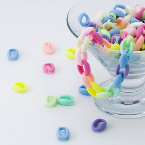 以下が含まれることがあります： カラフルなプラスチック製のチェーンリンクで満たされたガラスのボウル。リンクは、ピンク、ブルー、イエロー、グリーンなど、さまざまなパステルカラーです。いくつかのリンクは、白い表面のボウル周辺に散らばっています。