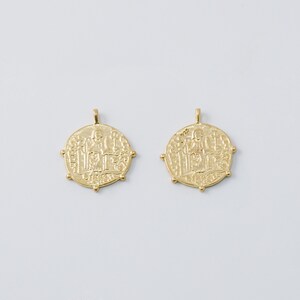 May include: Two gold-toned pendants shaped like round coins with intricate designs and raised edges.