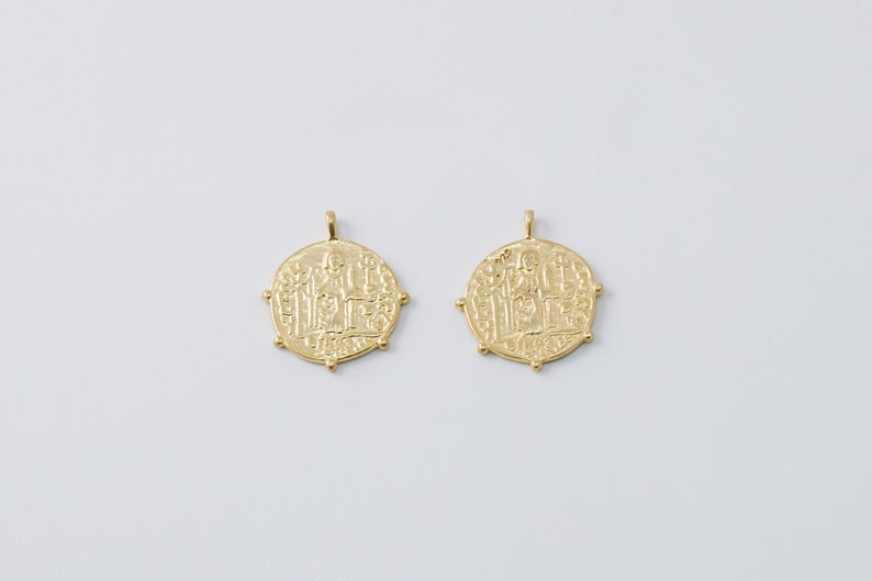 May include: Two gold-toned pendants shaped like round coins with intricate designs and raised edges.