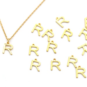 May include: A gold chain necklace with a gold letter R pendant. There are 11 additional gold letter R charms scattered around the necklace.