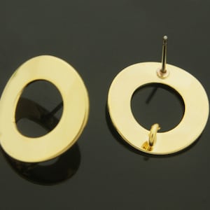 Puede incluir: Un par de pendientes de color dorado con un diseño circular. Los pendientes tienen un cierre de poste.
