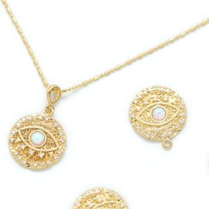 Puede incluir: Collar de oro con un colgante con un diseño de ojo turco con una piedra de ópalo blanco. El colgante está rodeado de pequeñas piedras transparentes. Hay varios otros colgantes de ojo turco con piedras de ópalo blanco sobre un fondo blanco.