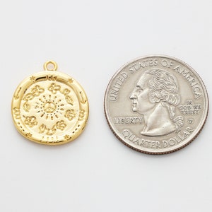 May include: A gold-toned pendant charm featuring a circular design with a peace symbol in the center surrounded by various symbols. The charm is about the size of a US quarter.