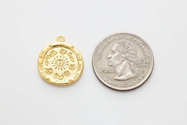 May include: A gold-toned pendant charm featuring a circular design with a peace symbol in the center surrounded by various symbols. The charm is about the size of a US quarter.