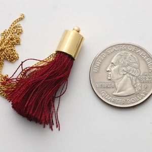 May include: A close-up of a small, burgundy tassel with a gold chain and a gold metal top. The tassel is about the size of a US quarter.