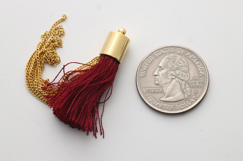 May include: A close-up of a small, burgundy tassel with a gold chain and a gold metal top. The tassel is about the size of a US quarter.