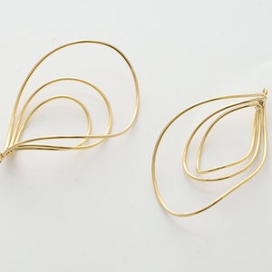 May include: A pair of gold-toned wire earrings with a teardrop shape. The earrings are made of multiple layers of wire, creating a delicate and intricate design.