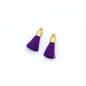 May include: Two purple tassel charms with gold metal tops.