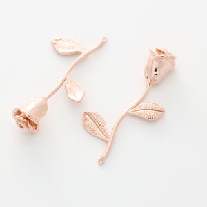May include: Two rose gold metal rose charms with stems and leaves. The roses are detailed and have a realistic look.