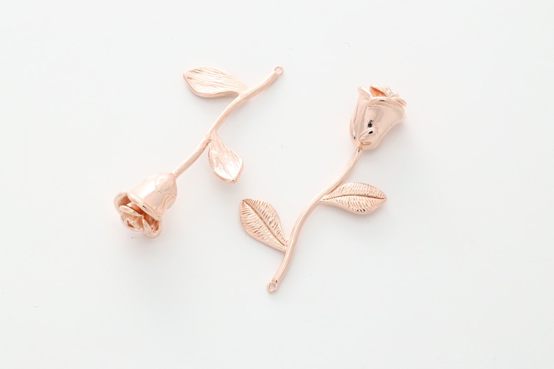 May include: Two rose gold metal rose charms with stems and leaves. The roses are detailed and have a realistic look.