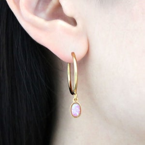 May include: Gold hoop earrings with a small, oval, pink opal pendant. The earrings are a simple, elegant design, perfect for everyday wear. The opal has a soft, pastel pink color.