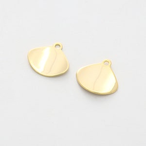 May include: Two gold-colored metal charms shaped like a scallop shell with a small hole at the top for attaching to jewelry.