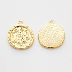 May include: Two gold-toned metal charms, one with a circular design featuring a sun with a peace sign in the center and the other with a textured surface.