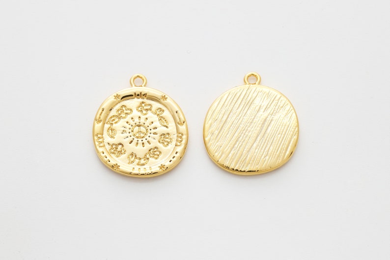 May include: Two gold-toned metal charms, one with a circular design featuring a sun with a peace sign in the center and the other with a textured surface.