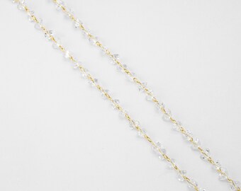 Könnte beinhalten: Eine zarte goldene Kettenkette mit klaren Kristallperlen. Die Kette besteht aus kleinen, miteinander verbundenen Goldmetallteilen, und die Perlen sind facettiert und haben eine klare, glasartige Optik.