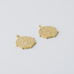 May include: Two gold-toned metal pendants with a raised design of figures. The pendants are round and have a loop at the top for attaching to a chain.
