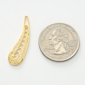 May include: A gold-colored metal pendant shaped like a teardrop with intricate cut-out designs. The pendant is about the size of a US quarter.