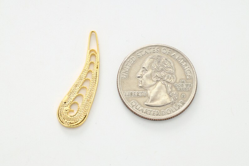 May include: A gold-colored metal pendant shaped like a teardrop with intricate cut-out designs. The pendant is about the size of a US quarter.
