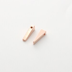 May include: Two gold-toned metal triangle shapes with a hole at the top. The shapes are different sizes and are on a white background.