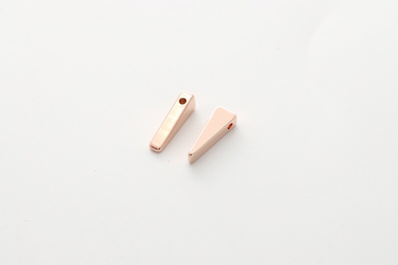 May include: Two gold-toned metal triangle shapes with a hole at the top. The shapes are different sizes and are on a white background.
