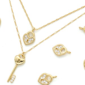 Puede incluir: Un collar de oro con un colgante de llave en forma de corazón y varios dijes de candado en forma de corazón, todos adornados con cristales transparentes brillantes.