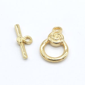 Peut inclure: Fermoir &agrave; bouton pression en m&eacute;tal dor&eacute; avec un motif en spirale. Le fermoir est compos&eacute; de deux pi&egrave;ces : une barre avec une boucle et un anneau avec un d&eacute;tail en spirale.