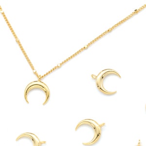 Op de afbeelding: Een gouden ketting met een halve maan hanger. De ketting is omringd door verschillende andere halve maan bedels.