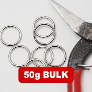 Op de afbeelding: Zilverkleurige sprongringen en een metale schaar met rode handvatten. Een rood rechthoek met de tekst "50g BULK" staat in de afbeelding. Voor knutselen.