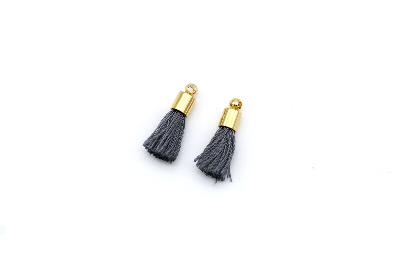 May include: Two gray tassel charms with gold metal tops.